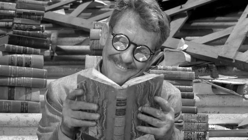 Cena do episódio 'Time Enough at Last' de The Twilight Zone, mostrando um homem com óculos quebrado em meio a livros.
