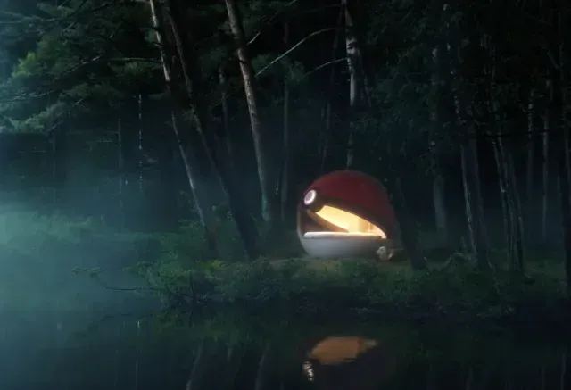 Exterior de um hotel com a forma de uma Pokébola gigante em meio a um cenário verde.